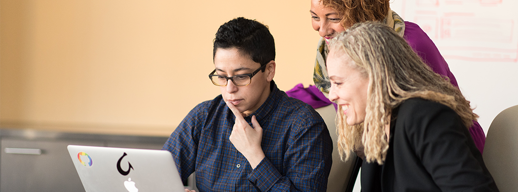 Three people reviewing an item on a laptop